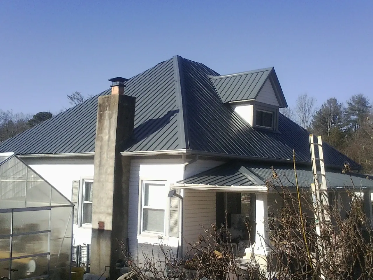 Dark blue standing seam metal roof on a white farmhouse with dormer — Slate & Tile Roof Repair by Roofing Brothers in Cement