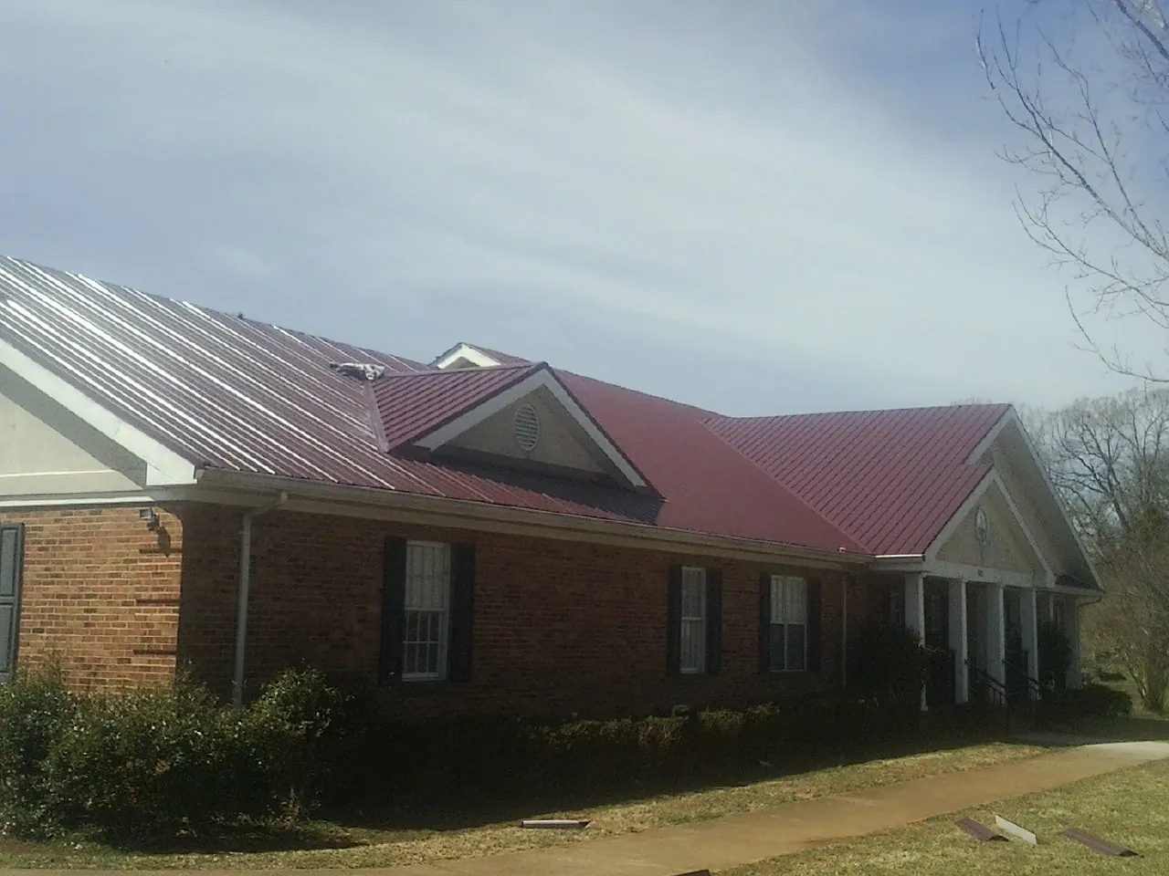 Red metal roof with gabled entries on a long brick building, from a Hail Damage Roof Repair job in Cement