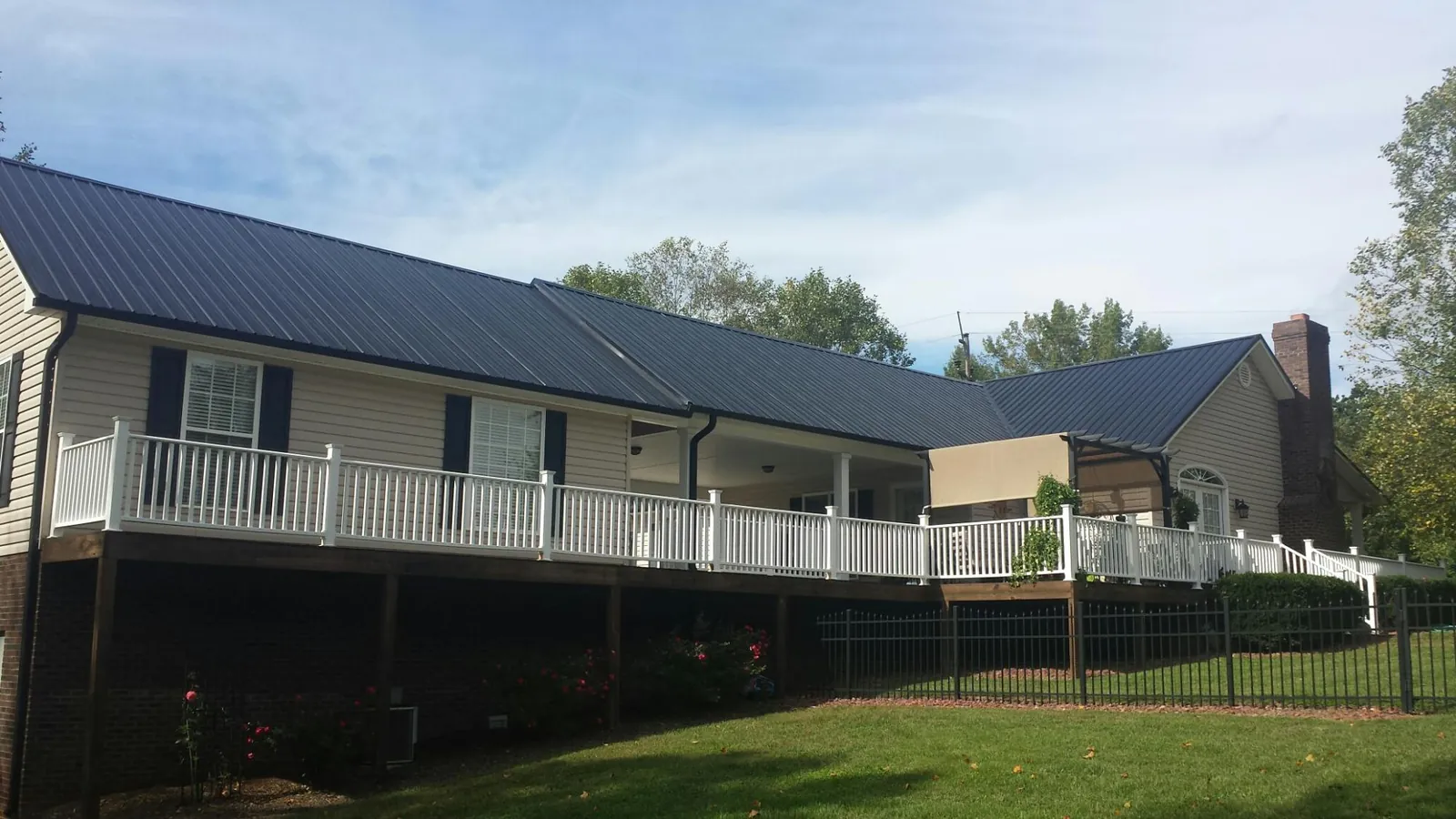 Black metal roof above a long white railed deck on a hillside home in Cement